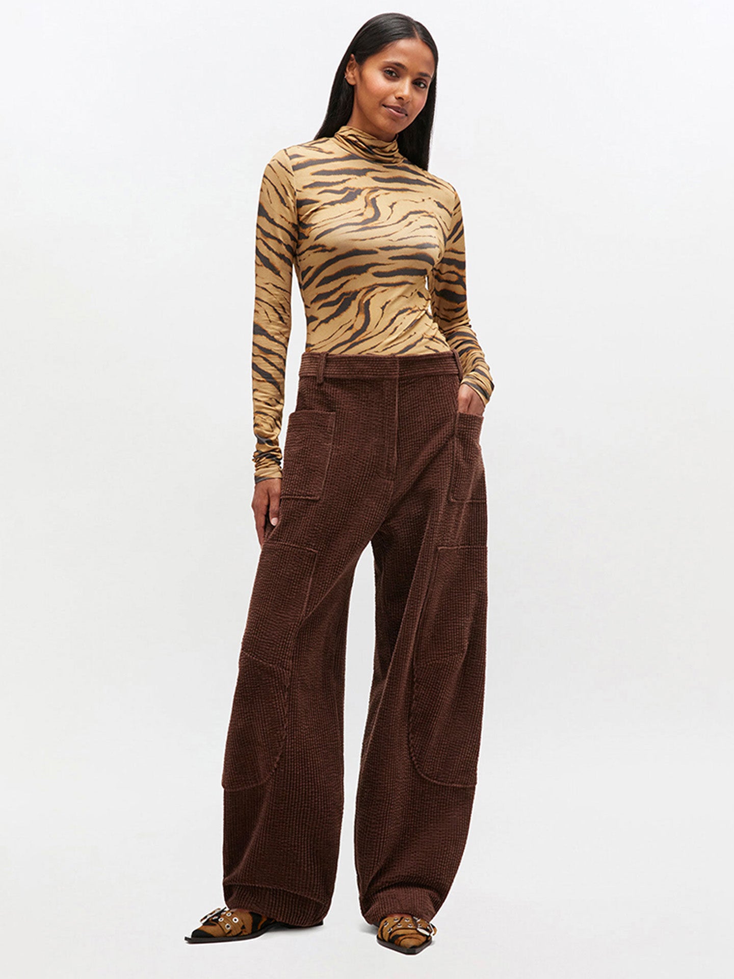 Woman wearing a tiger-striped long-sleeve top and brown corduroy pants on a white background