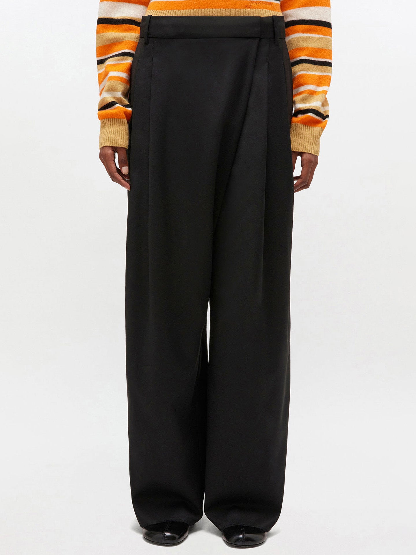 Person wearing black wide-leg pants with an orange and yellow striped sweater.