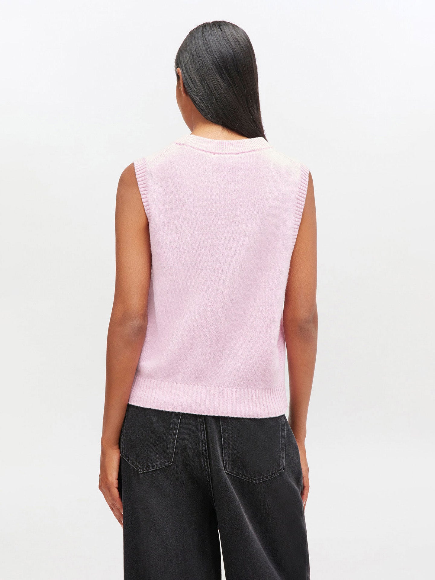 Person wearing a light pink sleeveless sweater against a white background
