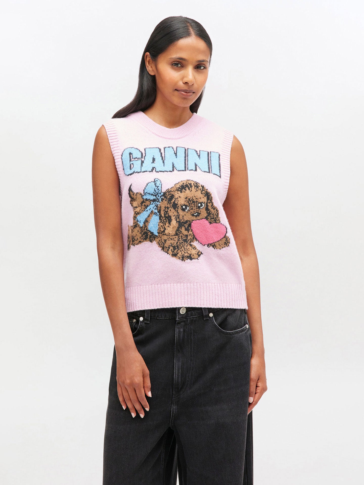 Woman wearing a pink sleeveless sweater with 'Ganni' branding and dog illustration on a white background
