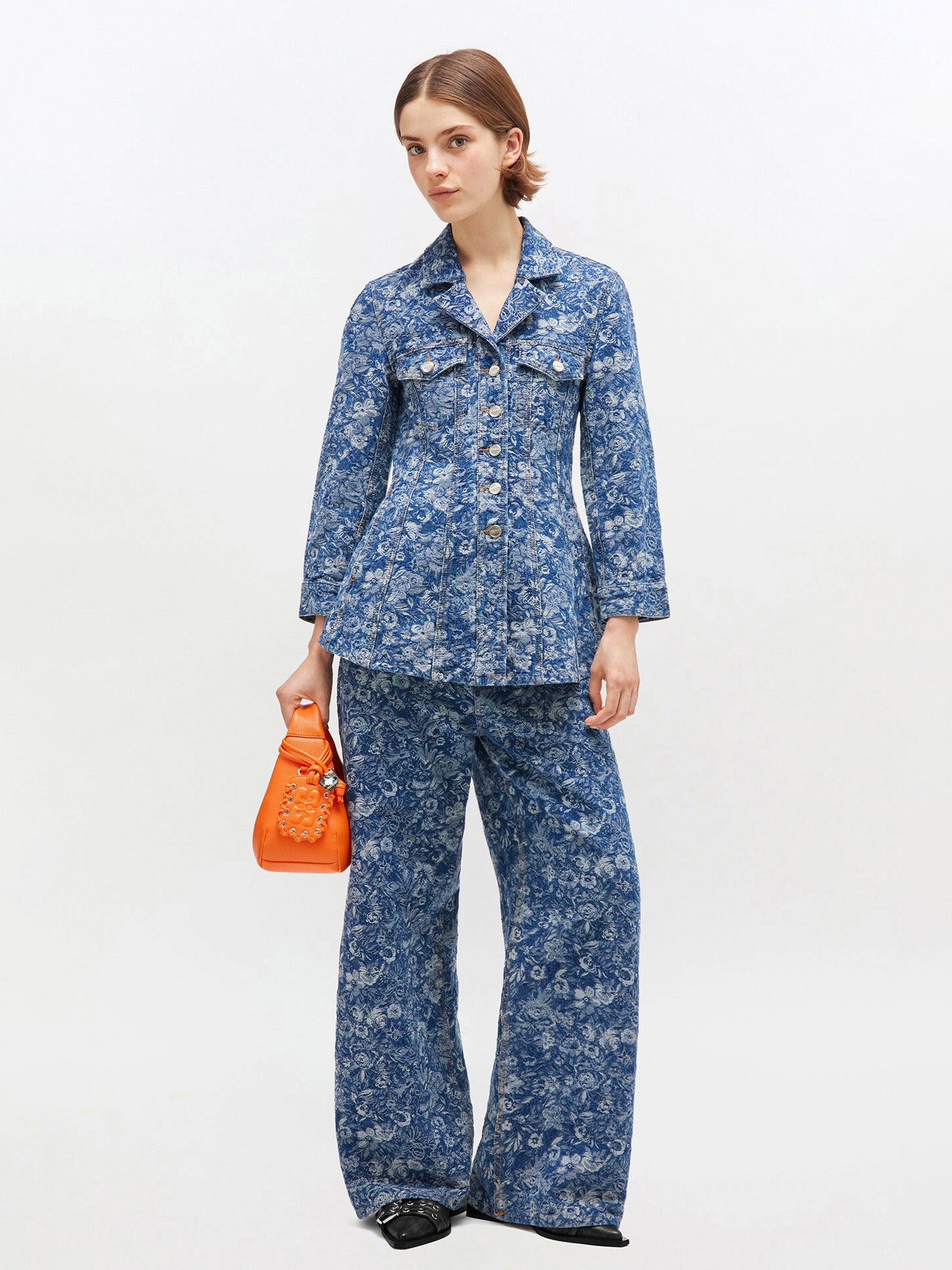 Woman wearing a blue floral outfit with an orange bag on a white background