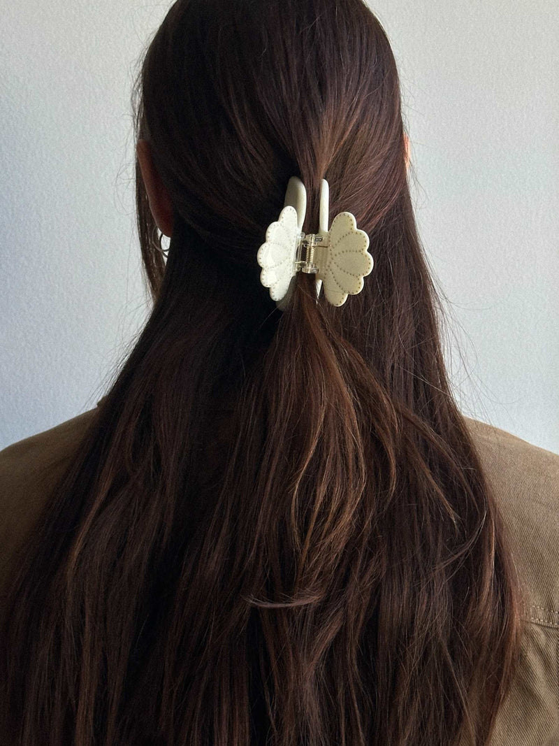 Person with long brown hair wearing a white floral hair clip against a plain background