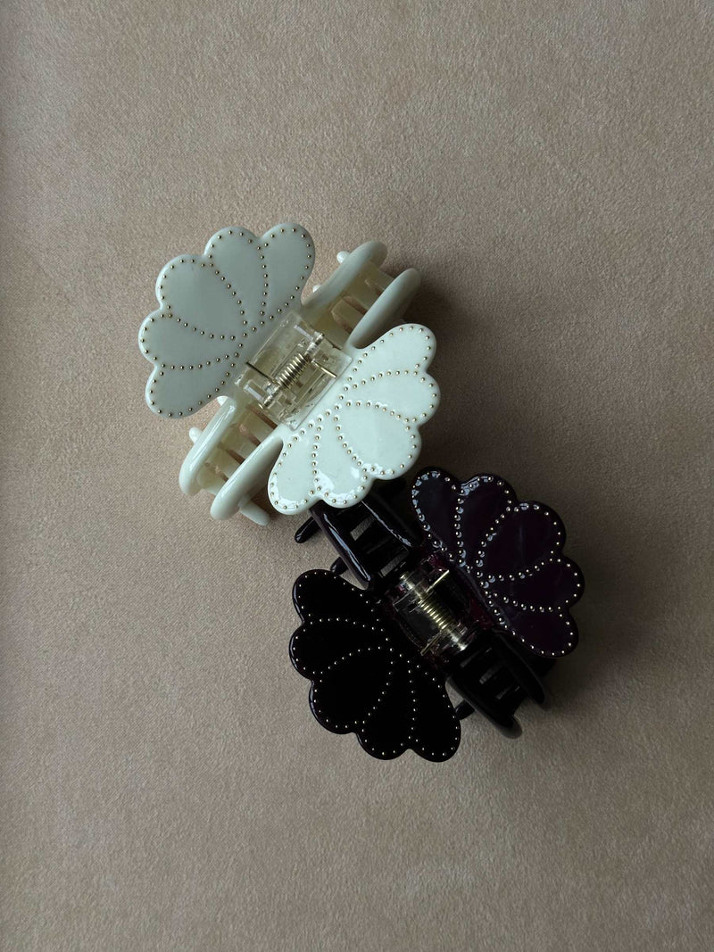 Two floral hair clips, one white and one black, on a beige background.