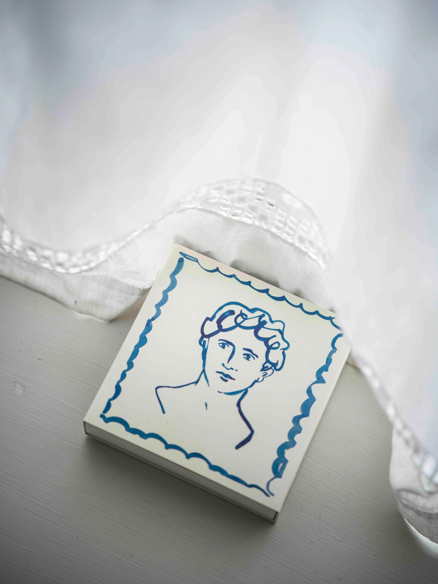 Small square tile with blue line art of a face on a white background