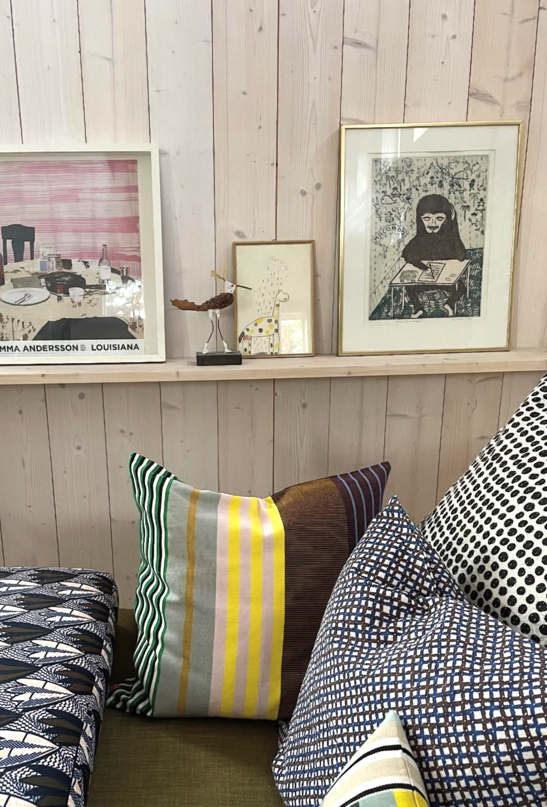 Decorative pillows on a sofa against a wooden paneled wall with framed artwork.