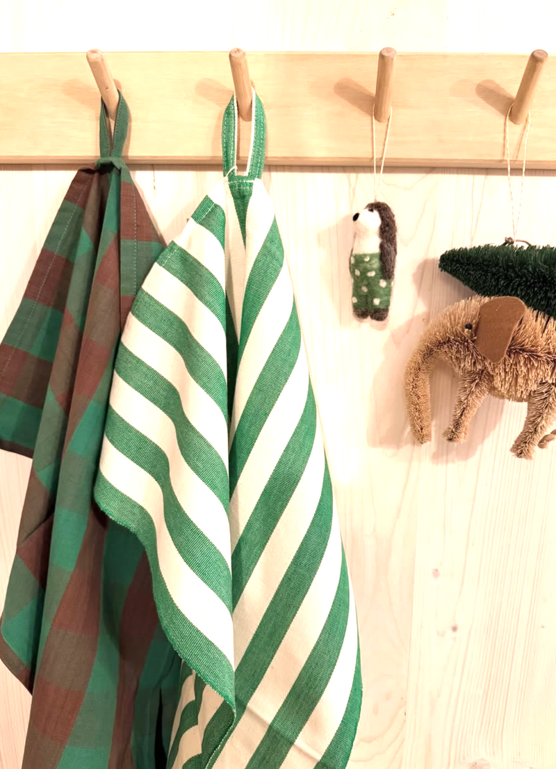 Green-brown gingham and white striped towels hanging on a wooden rack with a wooden wall in the background.
