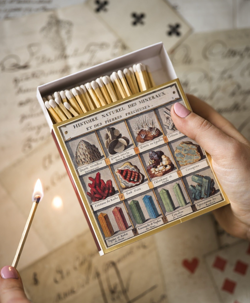 Matchbox with mineral illustrations held by a hand with a lit match.