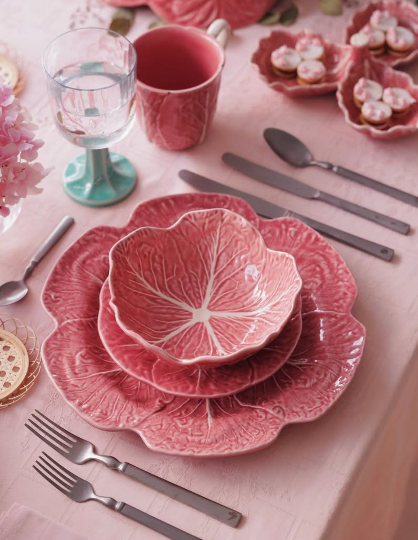 Pink ceramic cabbage plates on a table setting with cutlery and glasses.