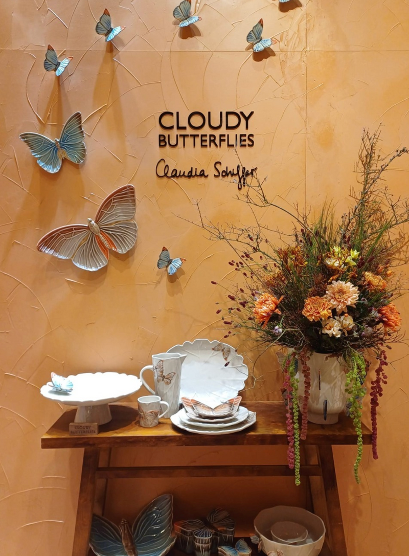 Decorative setting with butterflies, flowers, and ceramic items against a wall with 'Cloudy Butterflies' text.