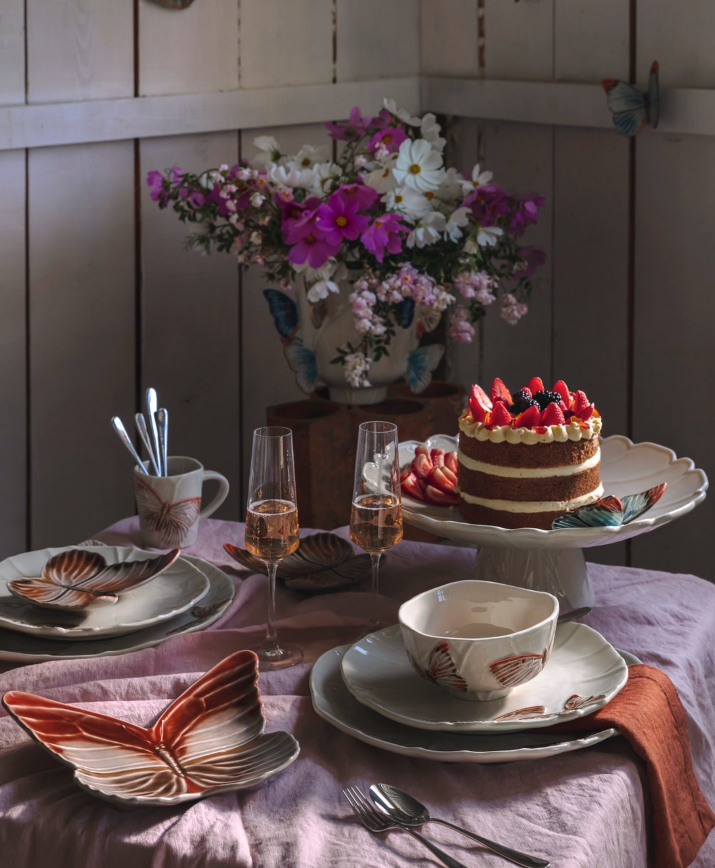 Dining table set with a cake, glasses, and floral arrangement in a cozy room.