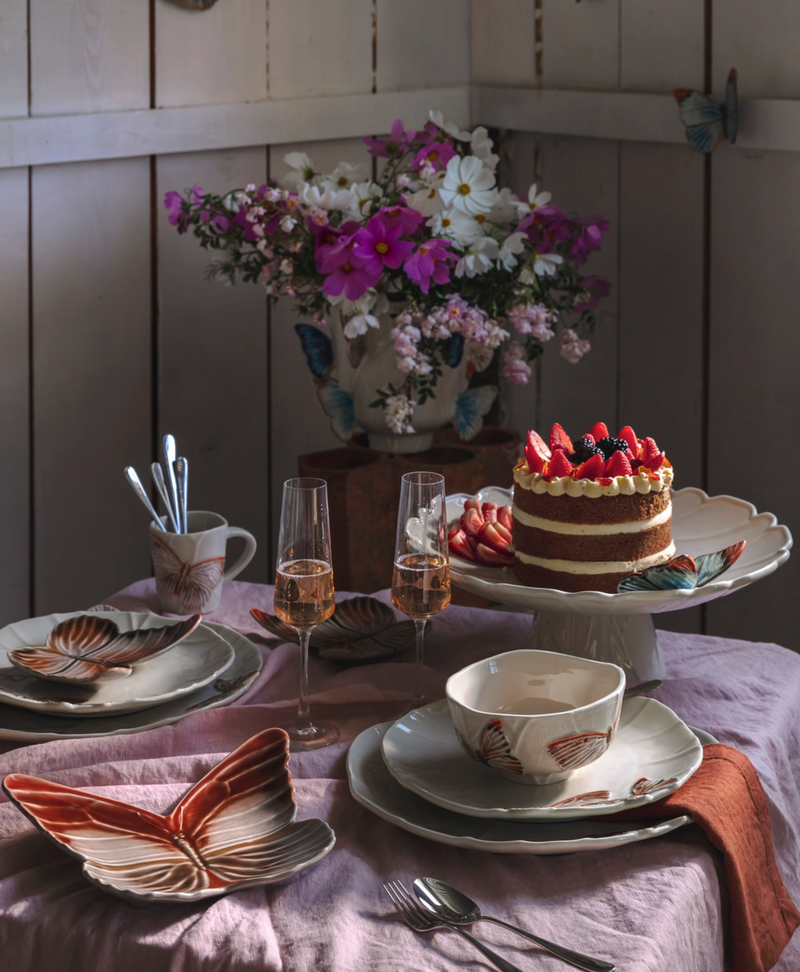 Dining table set with a cake, glasses, and floral arrangement in a cozy room.