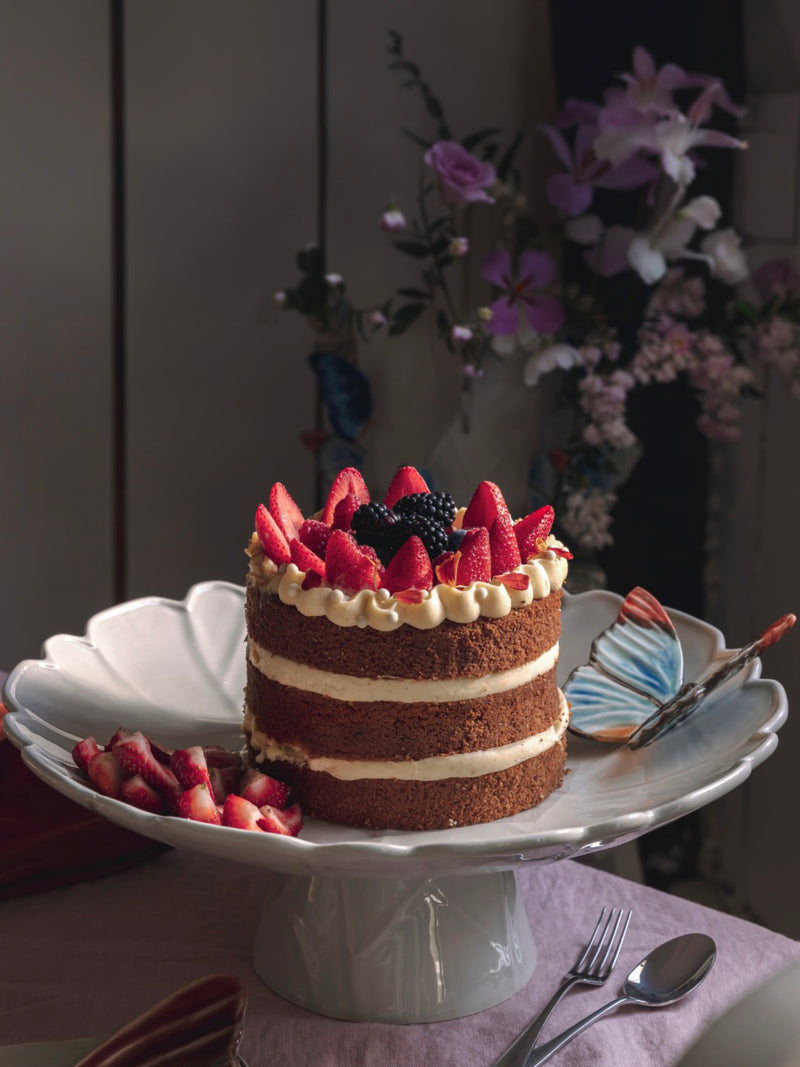 Cake with strawberries and cream on a decorative cake stand with butterfly relief.