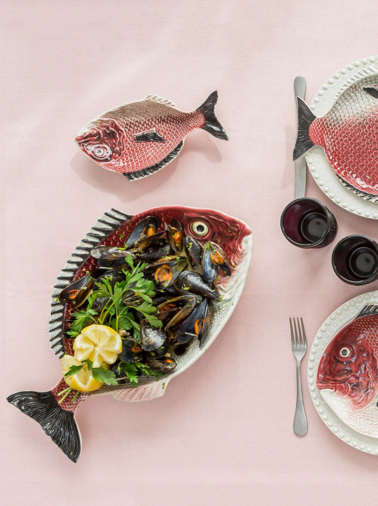 Decorative fish-shaped plates with mussels and lemon on a pink background
