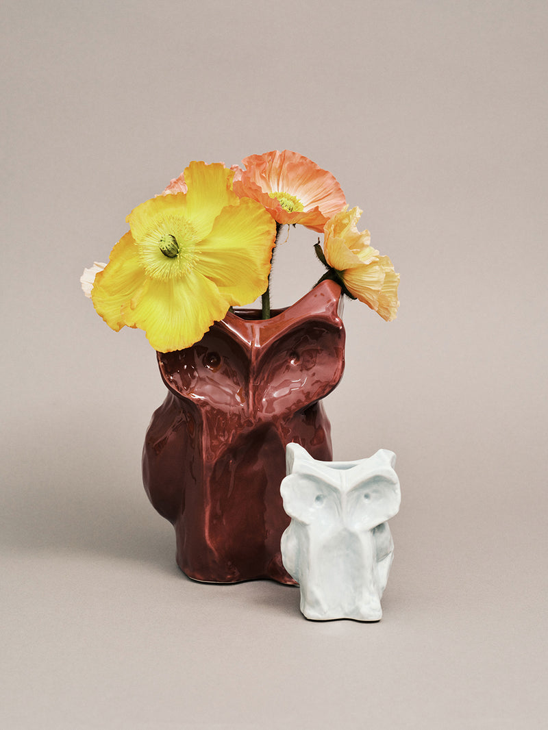 Owl vase with yellow flowers and a light blue owl-shaped object on a beige background