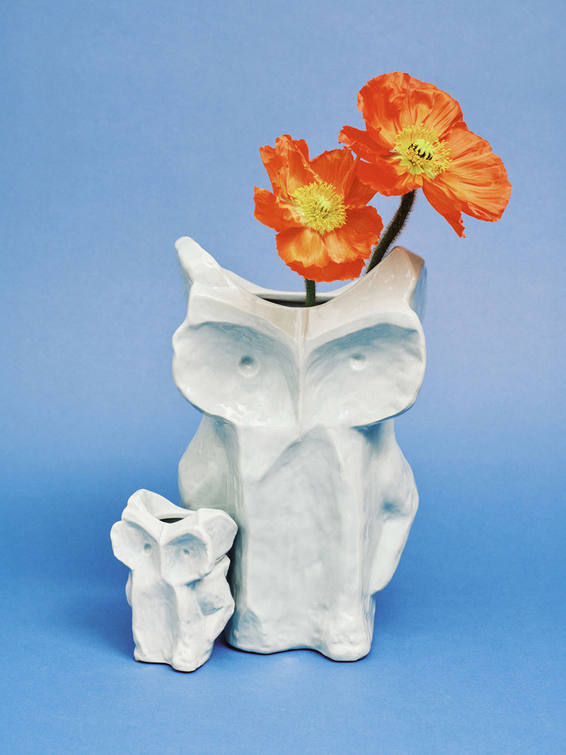 Light blue ceramic owl vase with orange flowers on a blue background