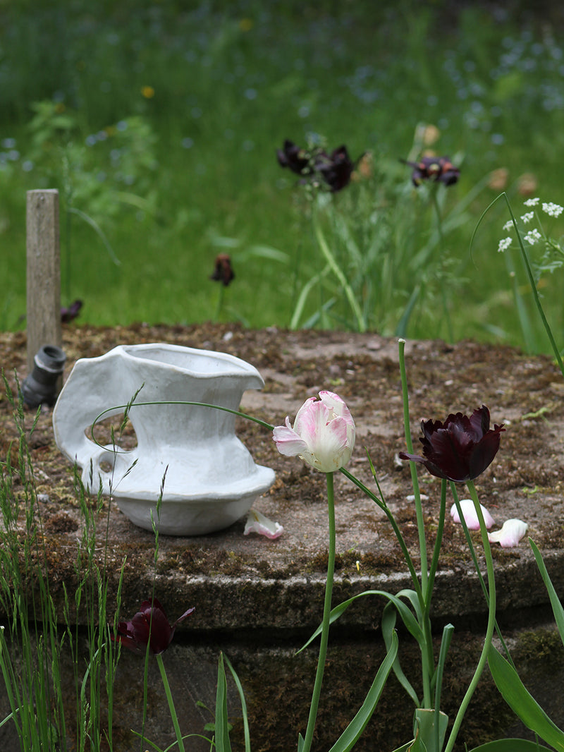 White ceramic jug on a stone surface with flowers and greenery in the background