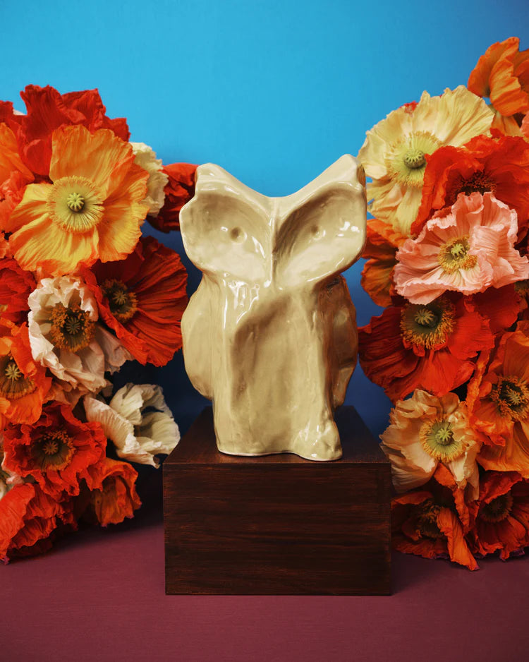 Ceramic owl head vase on a wooden base with colorful flowers against a blue and purple gradient background