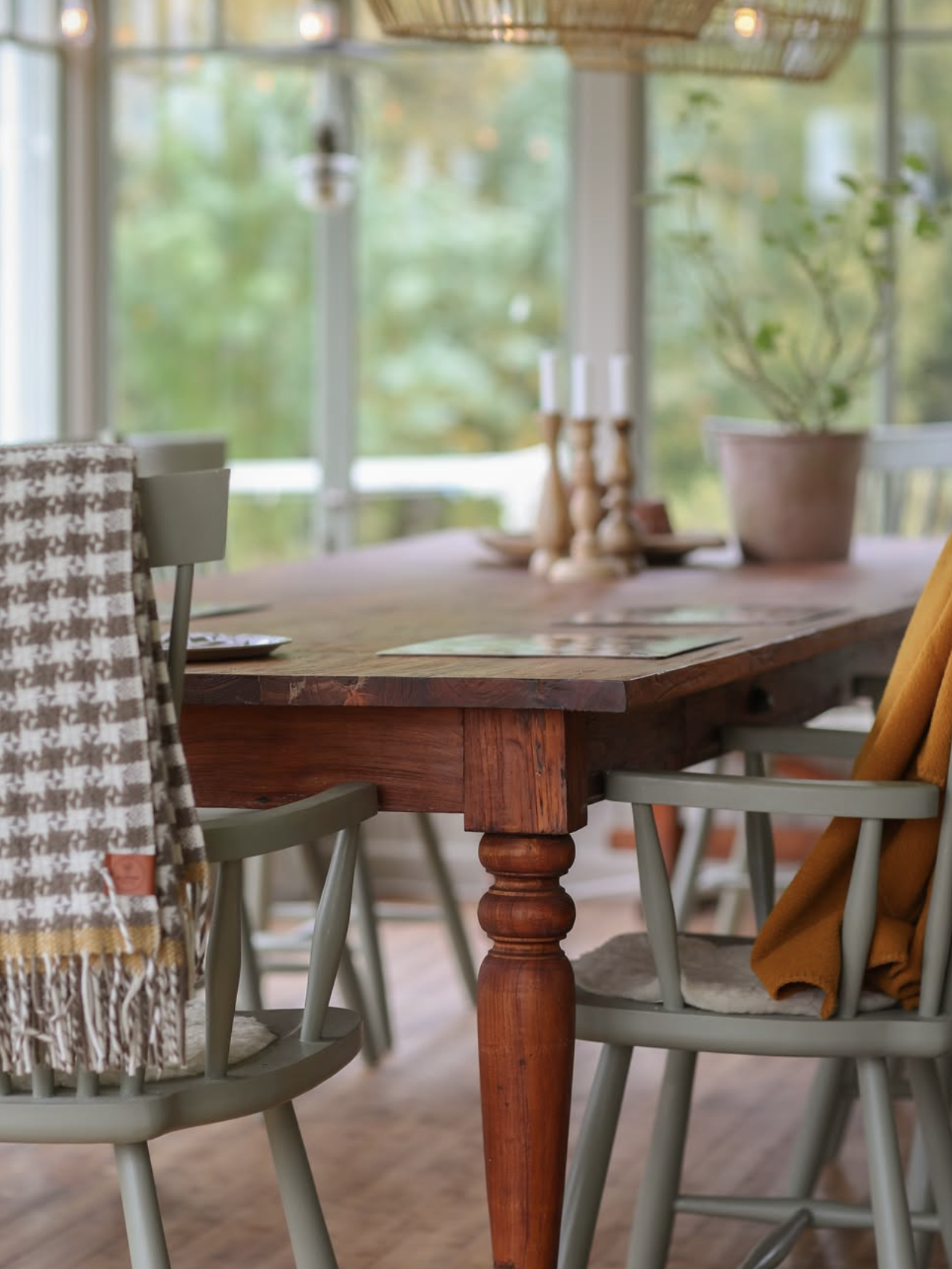 Dining room with wooden table and chairs near large windows with a view of greenery.