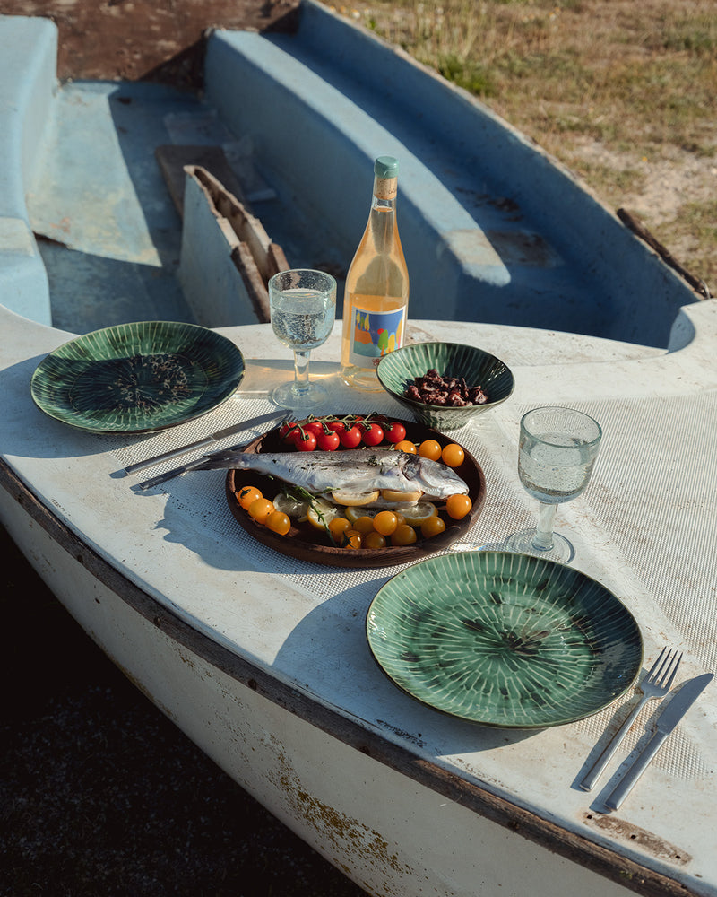 Dinner setup on a boat with plates, glasses, and a bottle of wine.