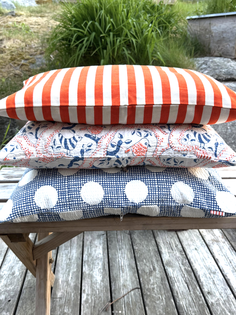 Stack of outdoor cushions with striped, patterned, and checkered designs on a wooden surface.