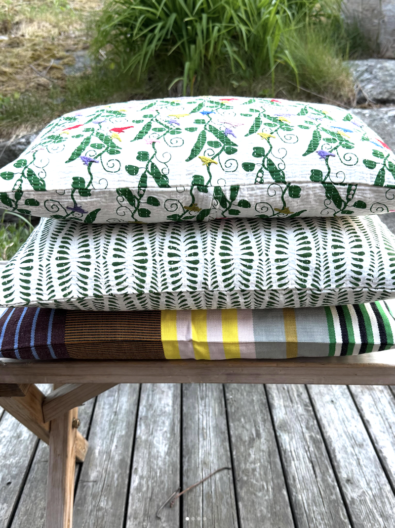 Stack of colorful fabric cushions on a wooden bench outdoors.