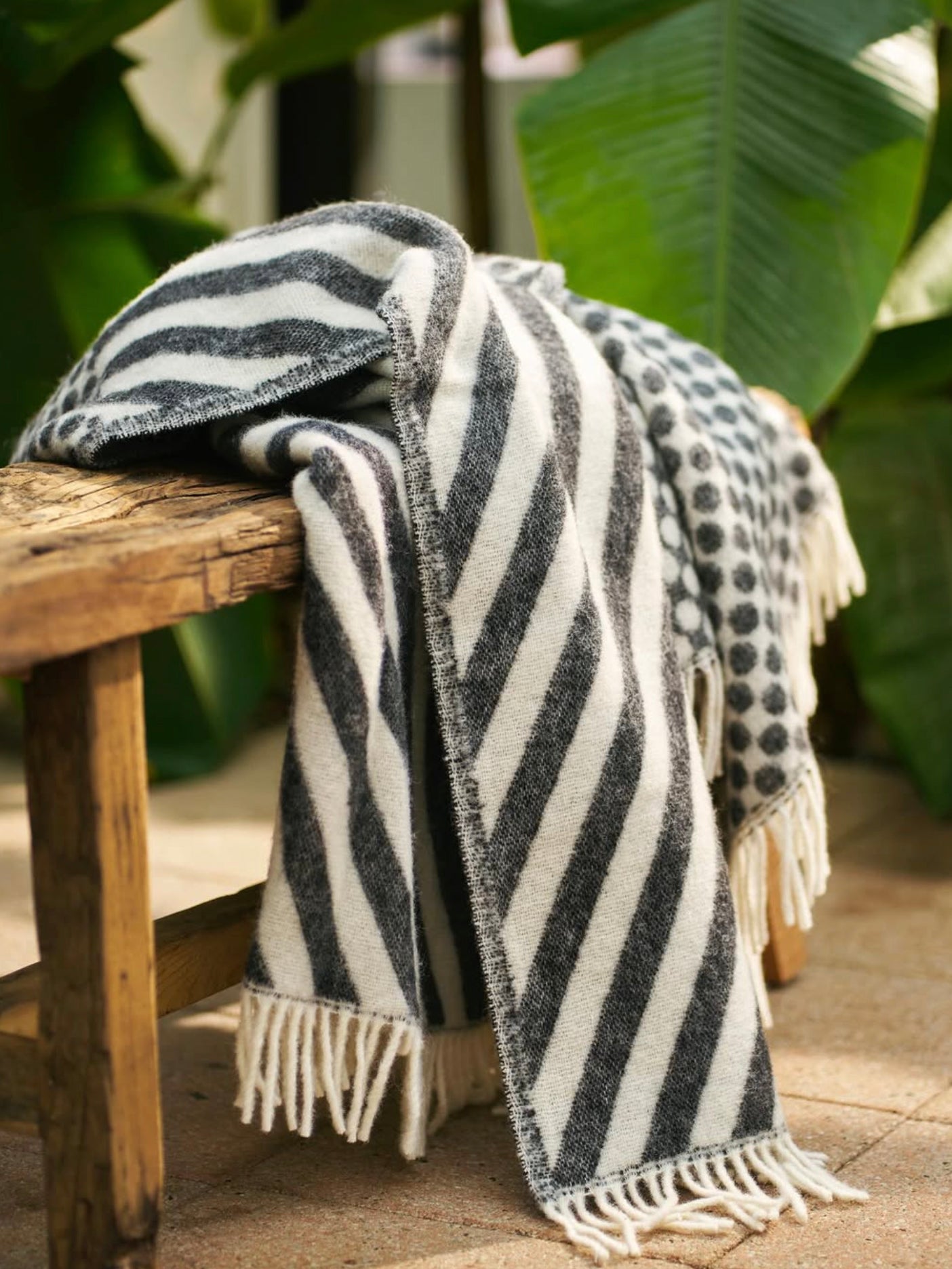 Striped wool throw draped over a wooden bench with green foliage in the background