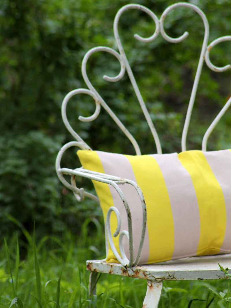 White metal bench with a yellow and pink striped cushion in a garden setting