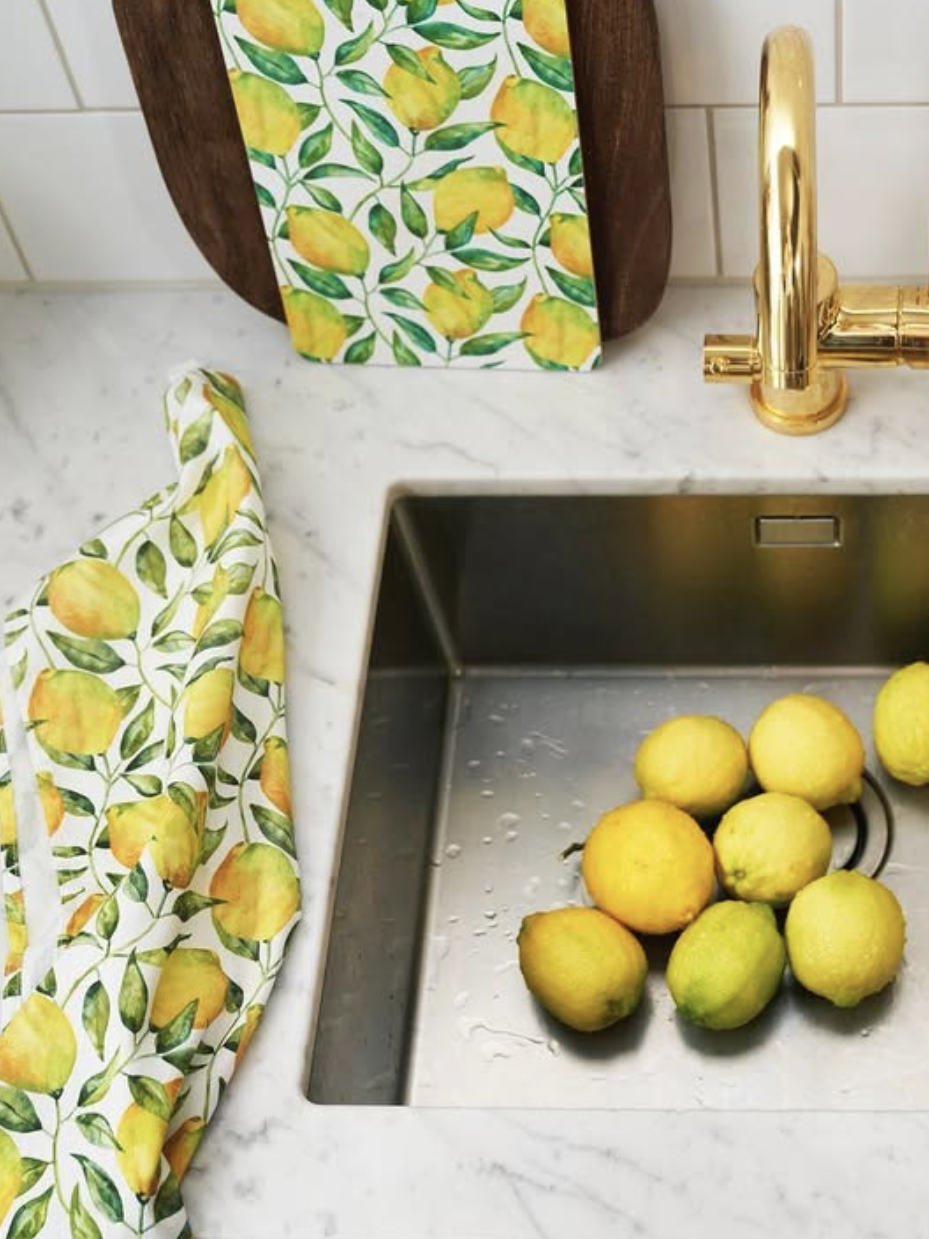 Kitchen sink with lemons and lemon-patterned towels on a marble countertop.