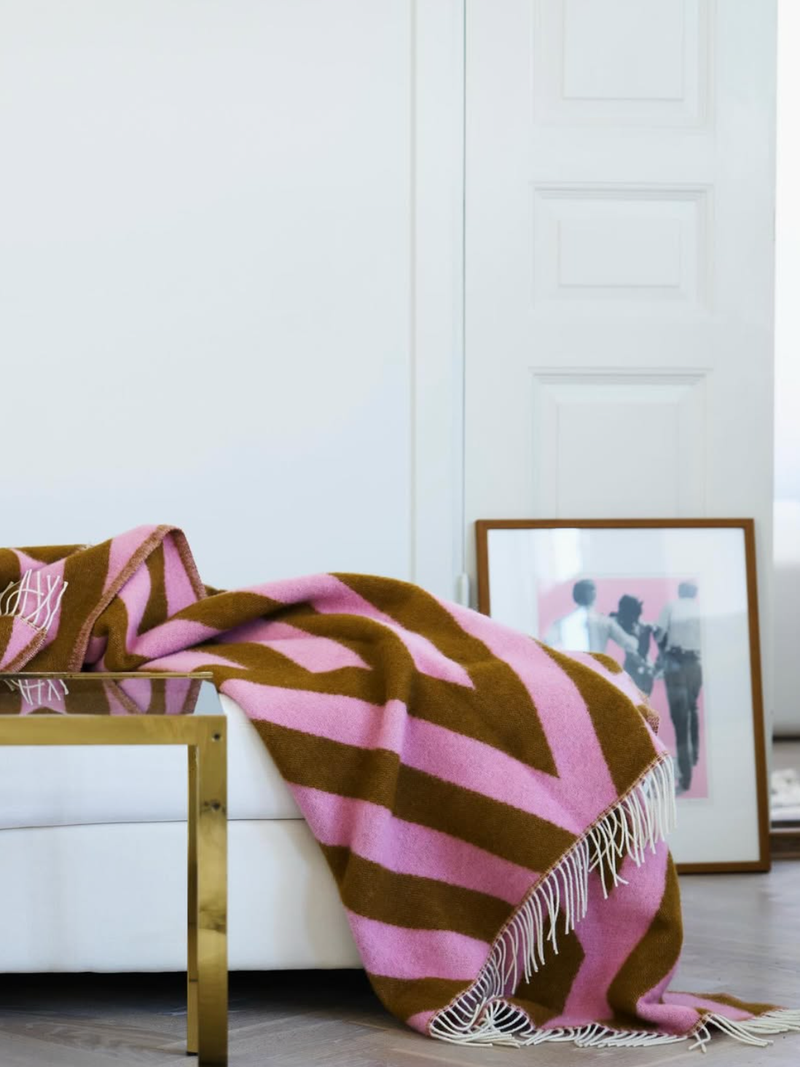 Pink and brown diamond patterned blanket with fringes draped over a white sofa with a framed picture in the background.