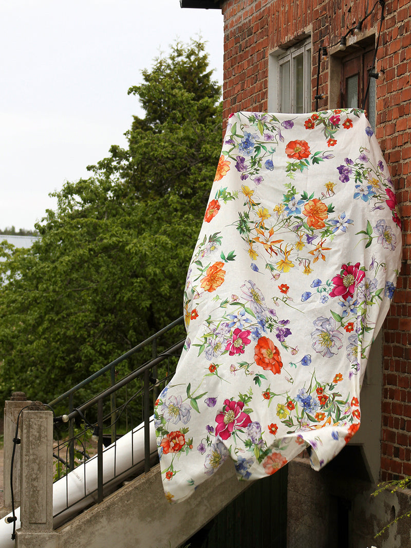 Floral-patterned tablecloth hanging on a brick building with greenery in the background