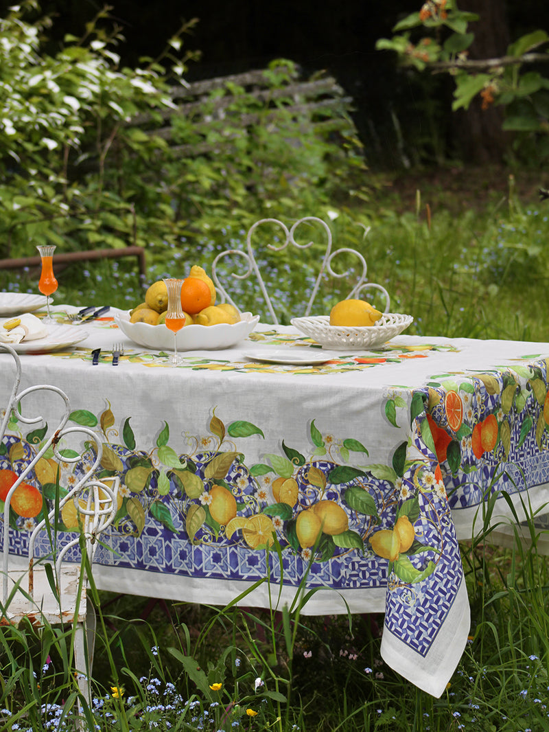 Outdoor table setting with a decorative tablecloth featuring lemons and oranges in a garden.