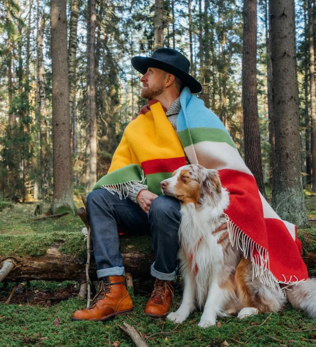 Man sitting in a forest with a colorful blanket and a dog