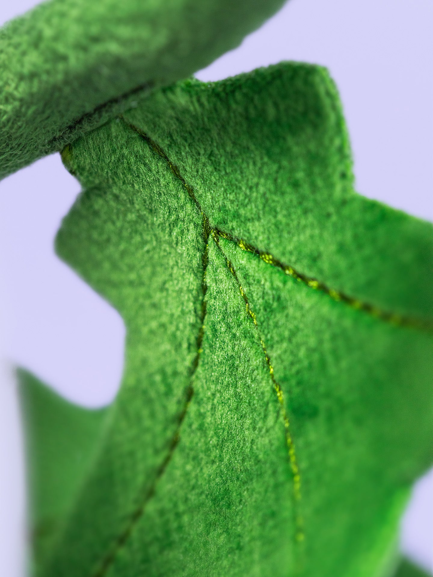 Close-up of a green fabric leaf with stitching details on a light blue background