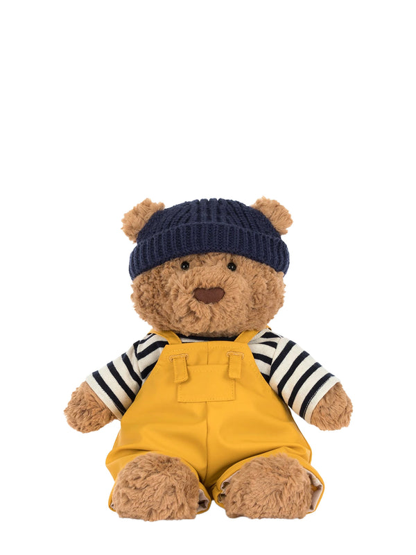 Teddy bear wearing a navy hat and yellow overalls with a striped shirt on a white background