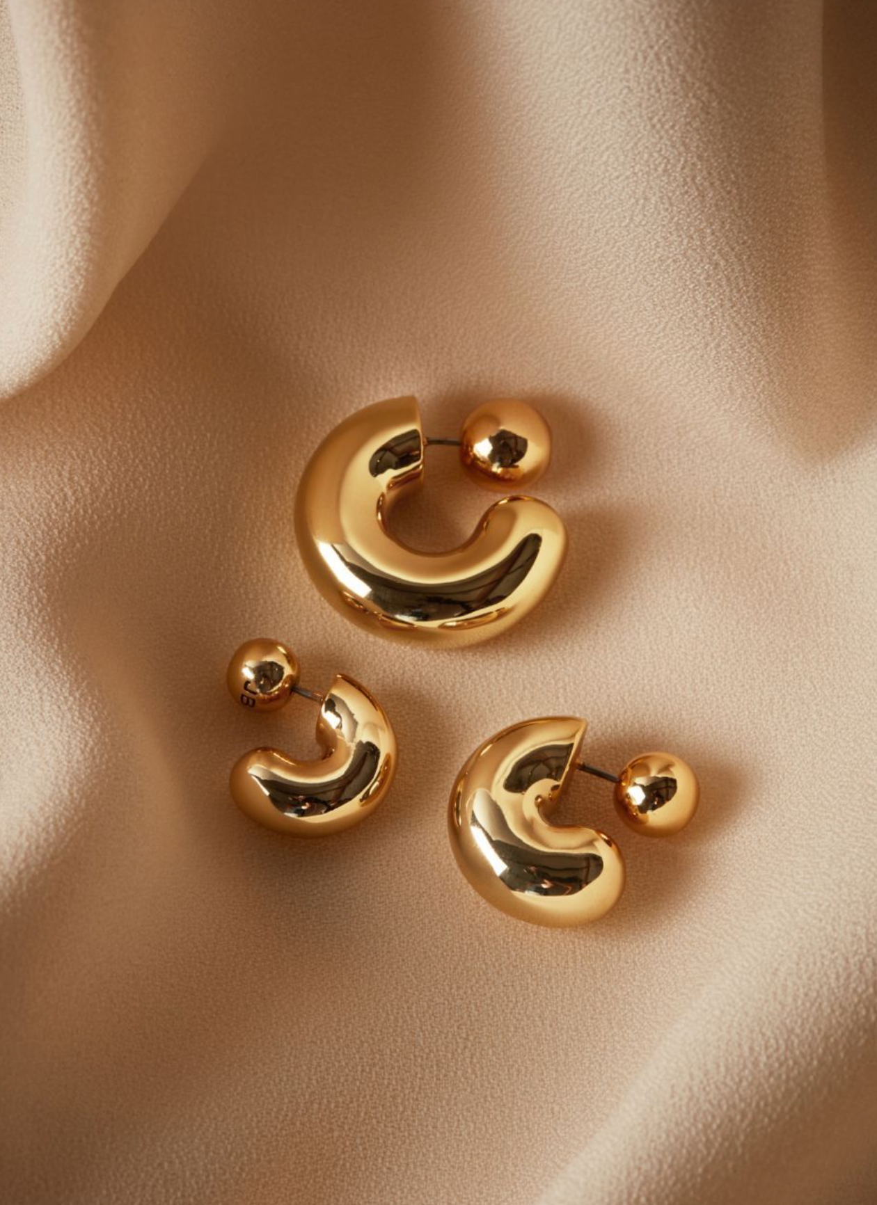 Gold crescent-shaped earrings on a beige fabric background