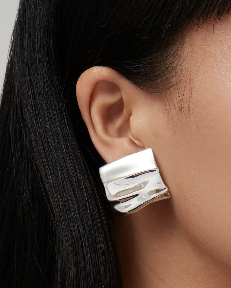 Silver earring worn by a person with dark hair on a neutral background