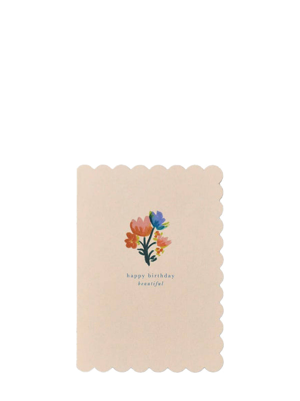 A rectangular beige pink greeting card with scalloped edges, featuring a small watercolor floral bouquet in orange, blue, and pink above the words 'happy birthday beautiful' in a light blue font, shown on a plain white background.