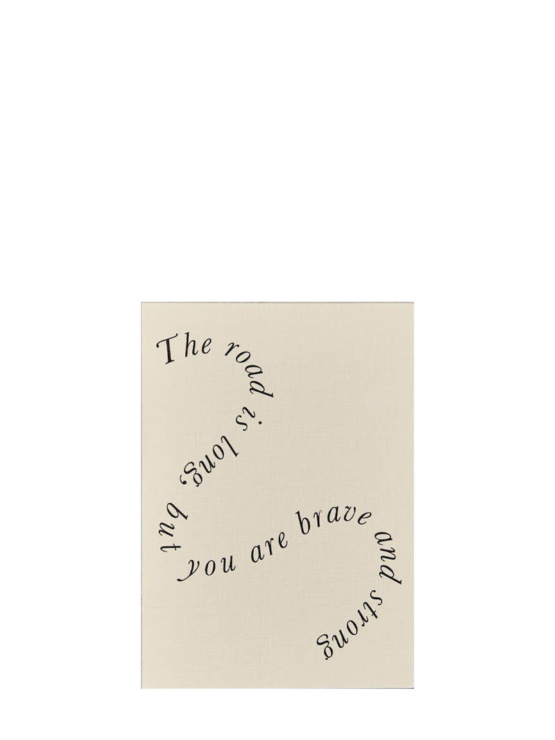 A square cream-colored greeting card with black cursive text reading 'The road is long, but you are brave and strong' on a plain white background.