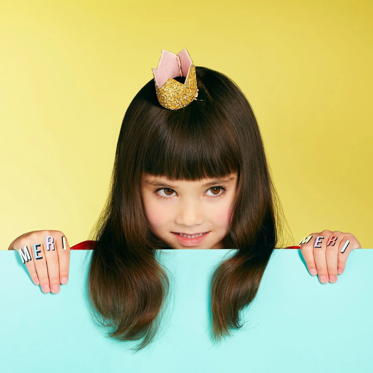 Child with decorative headband and colorful letters on a yellow and blue background