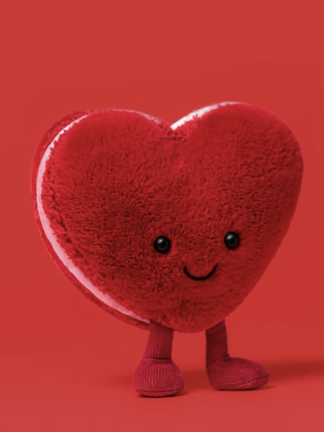Heart-shaped plush toy with a smiling face on a red background