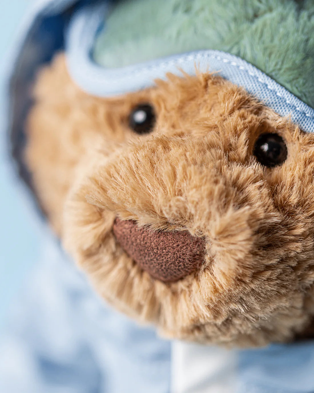 Close-up of a teddy bear with a blue bandage on its head against a light blue background