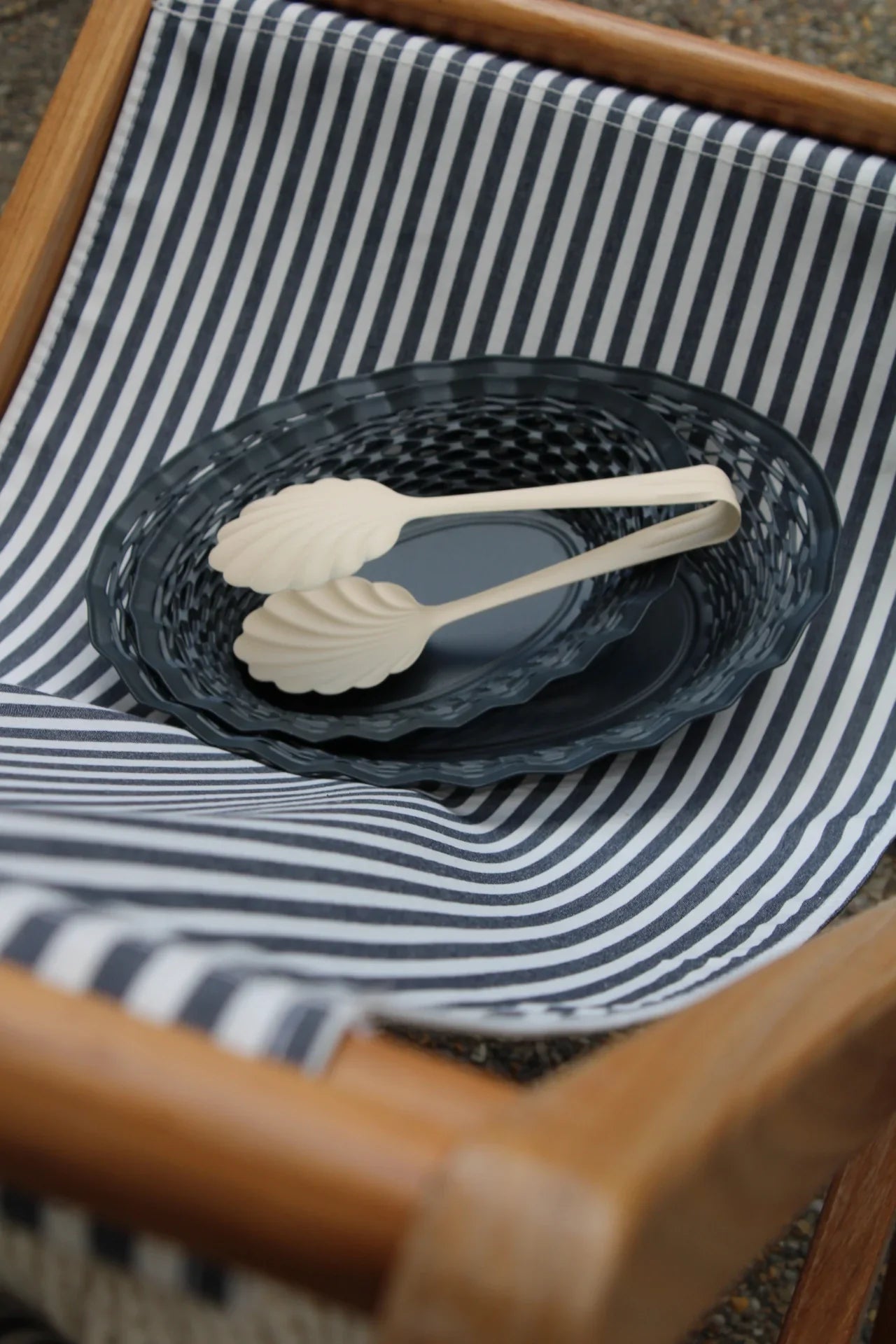 Set of salad tongs on a dark metal basket with a striped fabric background
