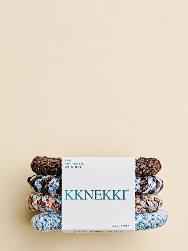 A stack of KKNEKKI braided hair ties wrapped in a white paper band, displayed on a solid beige background. The hair ties feature various color combinations including gingerbread brown, brown-baby blue mix, orange-baby blue-brown mix and baby blue.