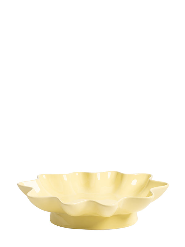 A pale yellow ceramic dish with a scalloped, flower-like rim and a small pedestal base, photographed on a plain white background.