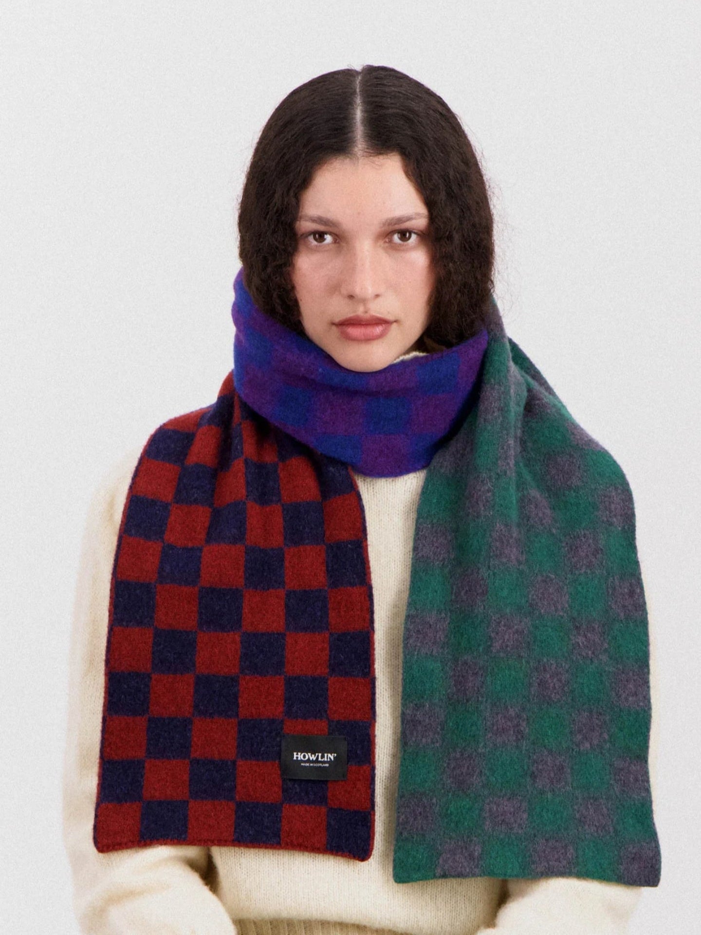 Person wearing a red and blue checkered scarf and a green and purple patterned scarf on a white background