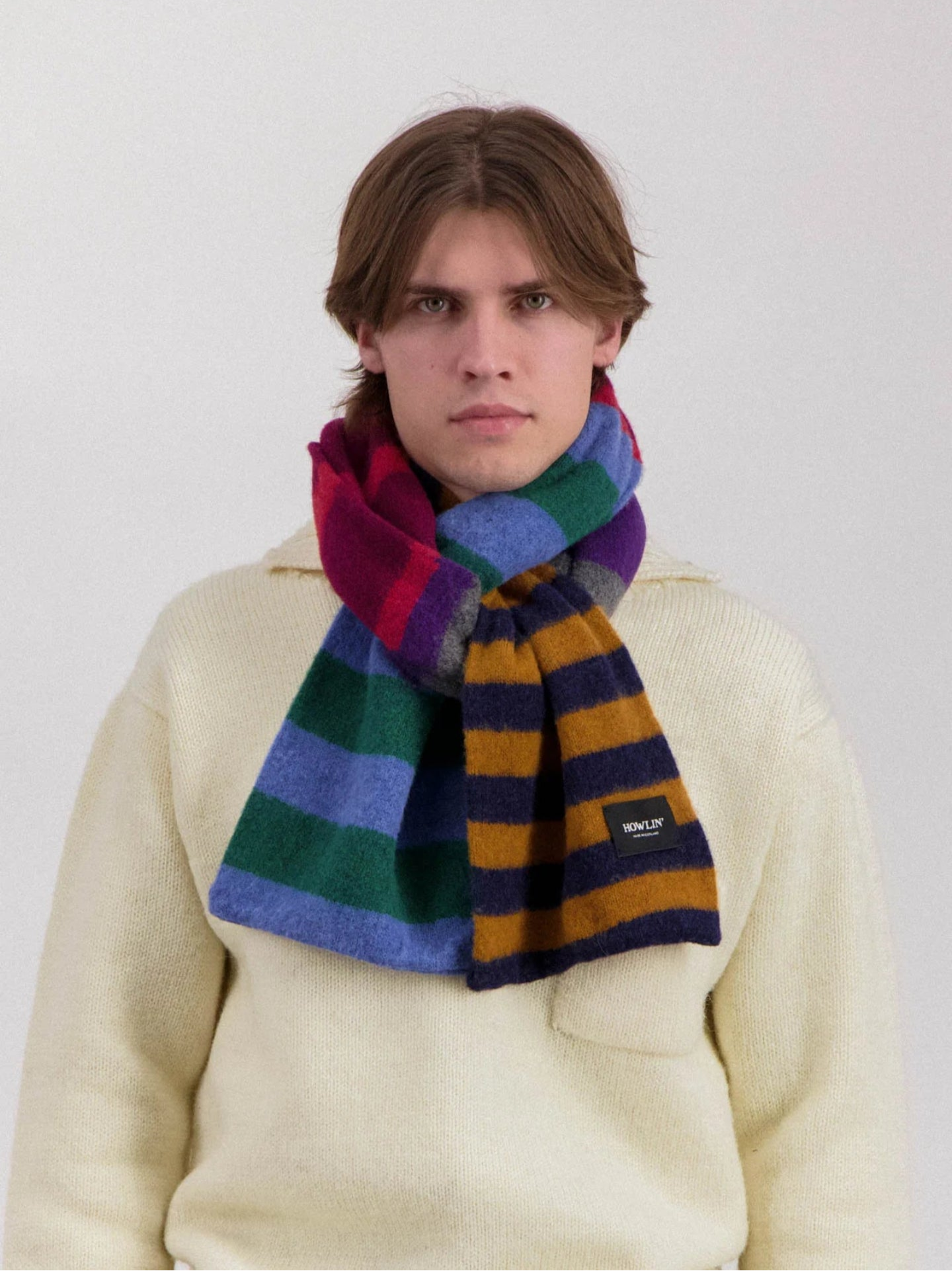 Person wearing a colorful striped scarf and beige sweater against a white background