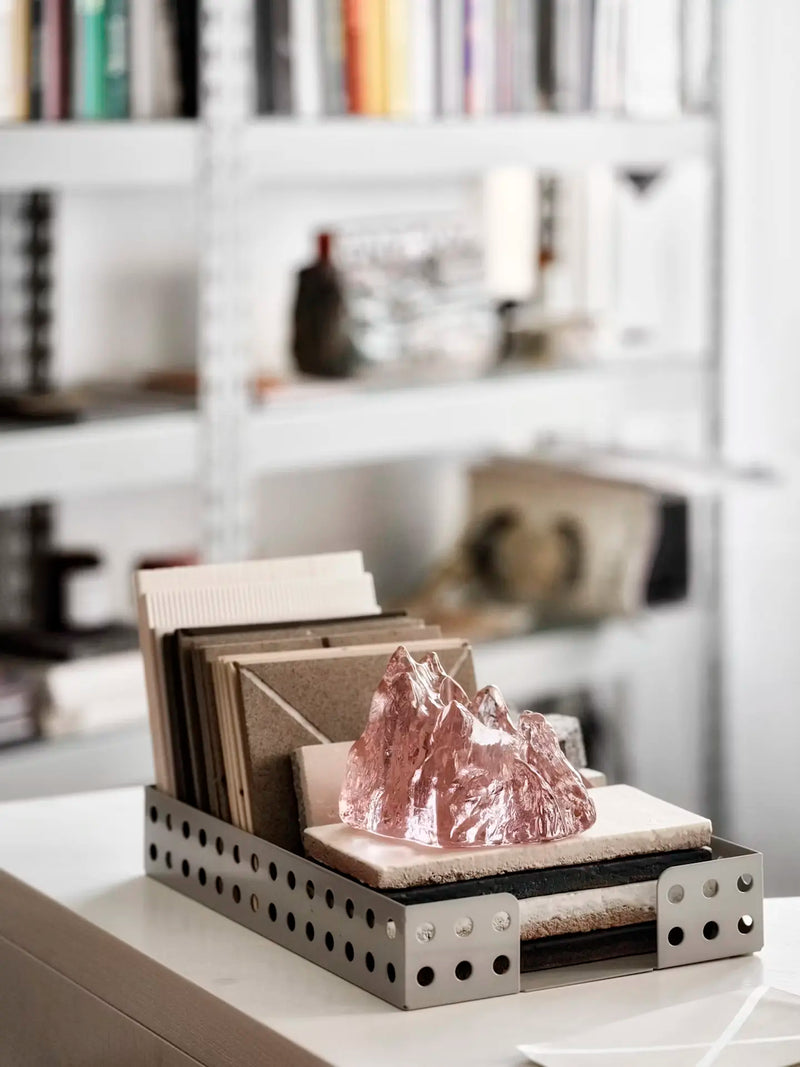 Decorative display with a crystal glass tealight holder resembling an ice-berg sitting on a tray propping up a set of tile samples in front of a bookshelf.