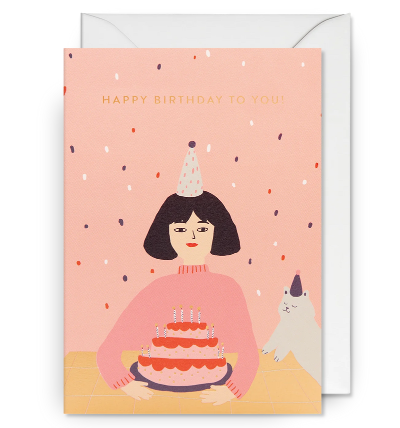 Illustrated birthday card with a person holding a birthday cake, a party hat on their head, and a dog looking on. The text 'HAPPY BIRTHDAY TO YOU!' is visible.
