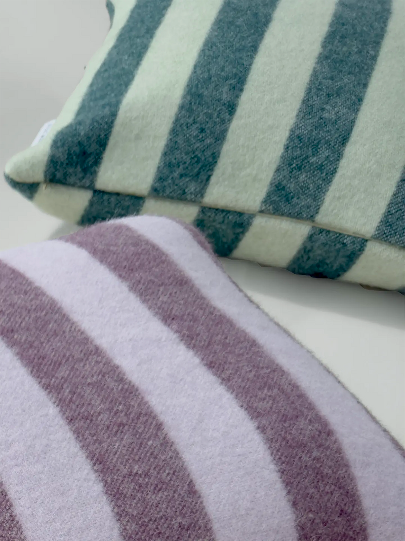 Two striped plush throw pillows shown close-up on a white surface, one in teal and matcha green stripes and one in dark mauve and pale lilac stripes.