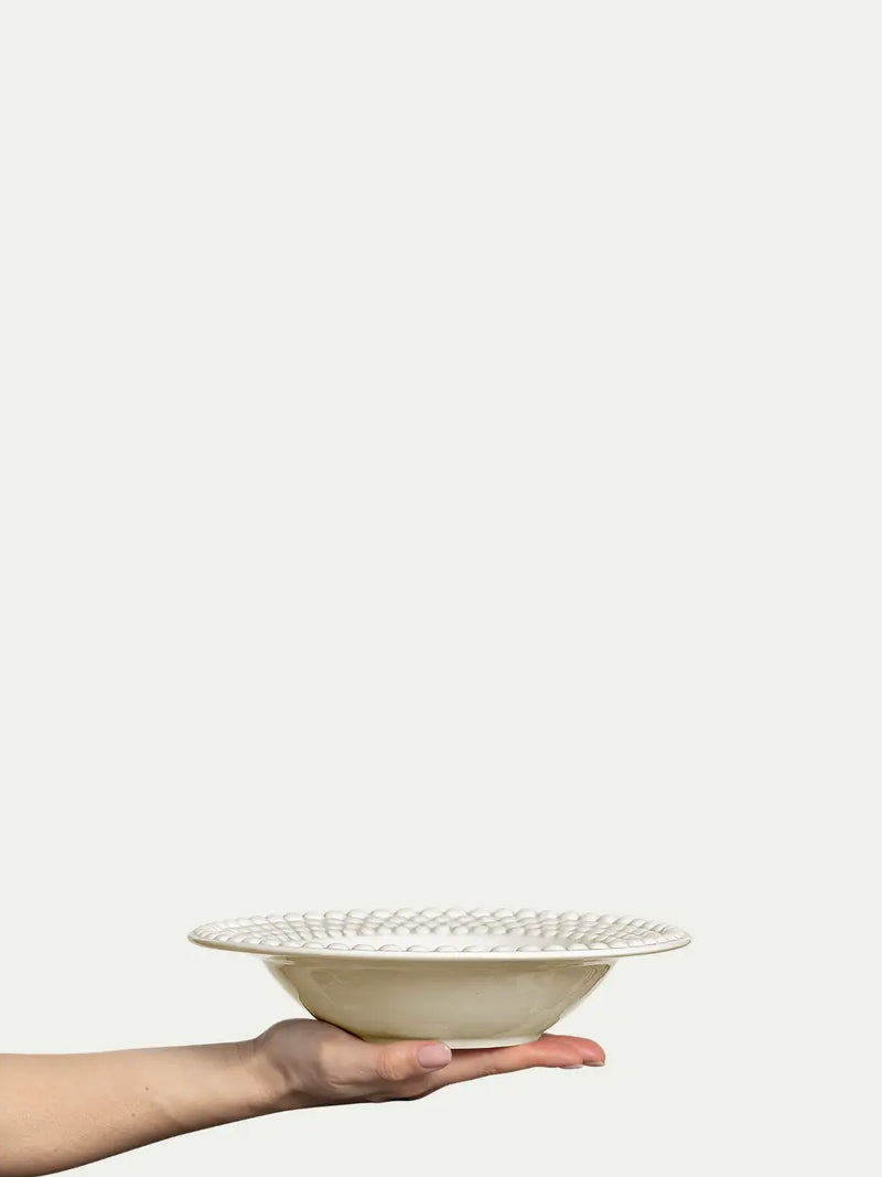 Hand holding a white ceramic bowl with decorative patterns on a light beige background